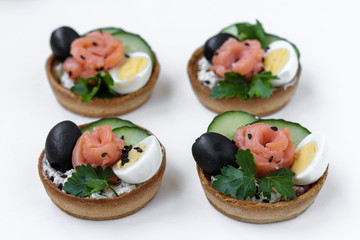 Holiday tartlets with cheese, salmon, black olives, quail eggs and cucumbers on white background, horizontal orientation