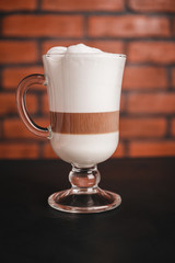 Glass with latte macchiato coffee on dark table, brick wall background