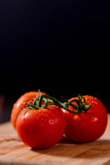 Close-up of fresh, ripe tomatoes on wood background. Vine tomatoes on black background. Tomato  with drops isolated on black, vertical space for text.