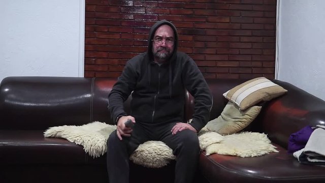 Bearded man switches the TV channels while sitting on the couch