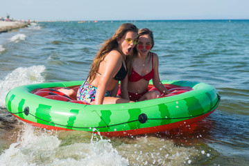 Happy friends two teenage girl floating with watermelon lilos, sea - Young trendy people having fun swimming in summer vacation - Youth lifestyle, travel and party concept