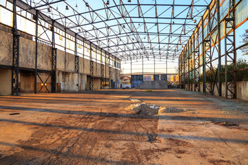Metal frame and concrete floor of demolished and partially dismantled industrial hall with clear blue sky as a backdrop, at sunset.