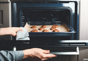 Woman putting baking tray with raw cookies in oven