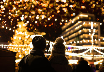 The couple are looking at the decorated Christmas market in the evening