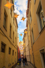 Cobblestone alley - narrow pedestrian street - with yellow houses and star shaped lanterns hanging above, in the old town of Riga, Latvian capital.