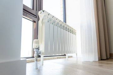 White big radiator with thermostat near window in modern room