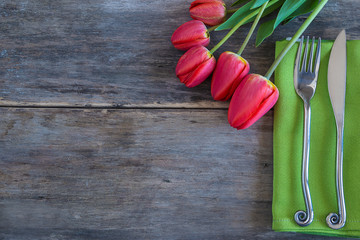 Festive place setting with fresh red tulips. Fork and knife on the green napkin and bouquet of red...