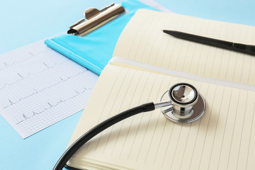 Stethoscope, notebook and cardiogram on color background. Cardiology concept