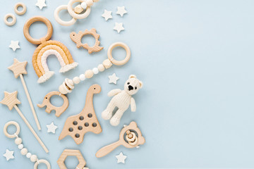 Cute wooden baby toys on light-blue background. Knitted bear, rainbow, dinosaur toy, beads and...