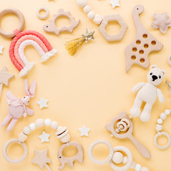 Cute wooden baby toys on yellow background. Knitted bear, rainbow, dinosaur toy, beads and stars. Eco accessories,  beanbag and teethers for newborn. Flat lay, top view