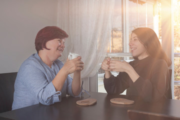 happy mother is chatting with her daughter, drinking coffee