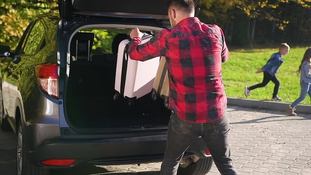 Handsome bearded modern man putting into car's trunk suitcases and boxes during moving into new home