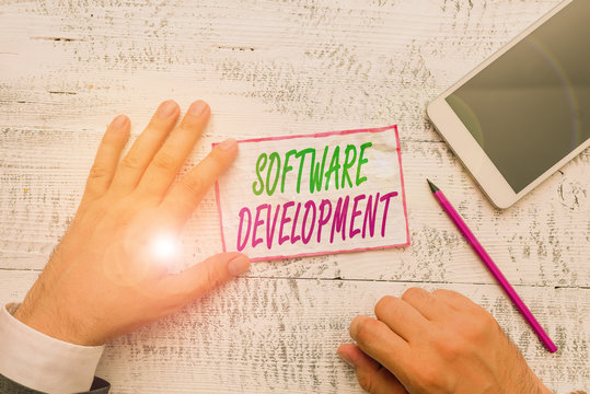Conceptual hand writing showing Software Development. Concept meaning software is created using a specific programming Hand hold note paper near writing equipment and smartphone