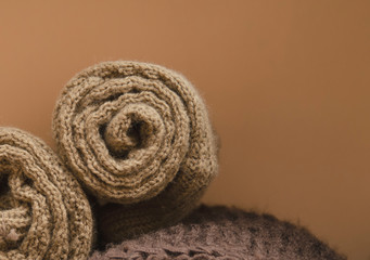 Knitted winter clothes twisted into tubes. Textile brown background.