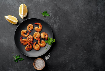 grilled shrimps, with lemons, herbs and spices, served on a black plate on a stone background with copy space for your text