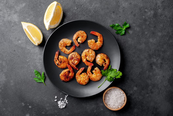 grilled shrimps, with lemons, herbs and spices, served on a black plate on a stone background 