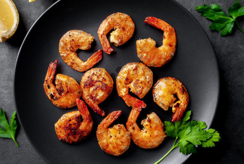 grilled shrimps, with lemons, herbs and spices, served on a black plate on a stone background 
