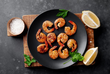 grilled shrimps, with lemons, herbs and spices, served on a black plate on a stone background 