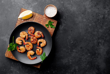 grilled shrimps, with lemons, herbs and spices, served on a black plate on a stone background with copy space for your text