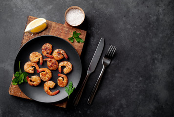 grilled shrimps, with lemons, herbs and spices, served on a black plate on a stone background with copy space for your text