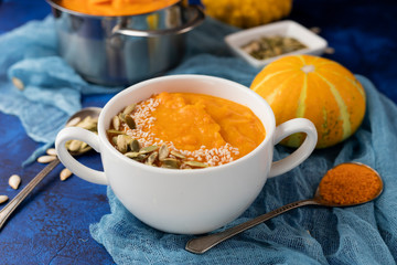 pumpkin cream soup in a white plate on a deep classic blue background with small decorative pumpkins with blue gauze and a spoon. flat lay.