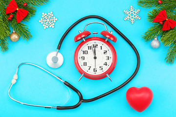 Branches of spruce, christmas toys, red heart with stethoscope and alarm clock with five minutes to twelve o'clock on a blue background. The concept of Christmas holidays and medical care.
