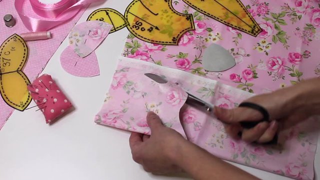 Handmade process. Hands cut out a pattern. Teddy bear head pattern. Pink cotton peas and flowers.