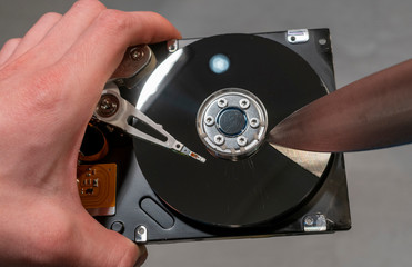Scratches a disassembled hard drive with a knife.
