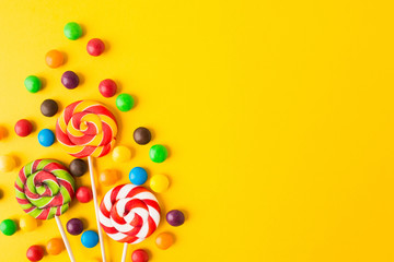 Three colorful round candies on sticks over yellow background with copy space. Closeup view