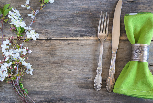 Festive place setting with twig of sakura. Vintage cutlery, green napkin with ring and twig of cherry on the old non paint wooden background. Flat lay, copy space