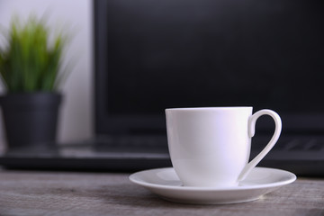  Cup of coffee on office desktop with laptop, computer on wooden table. Close up, with space for your text