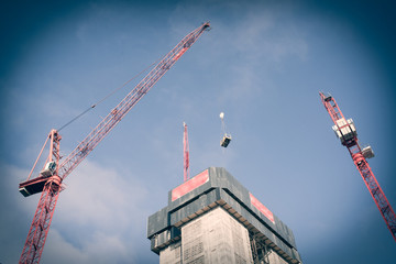 Two big red constuction cranes on building site in use. View from below.