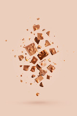 Flying in the air broken bar of milk chocolate with nuts and flakes on pastel pink background.  Chocolate pieces levitation concept.