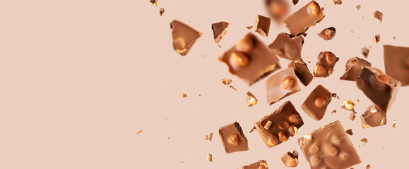 Flying in the air broken bar of milk chocolate with nuts and flakes on pastel pink background. ...