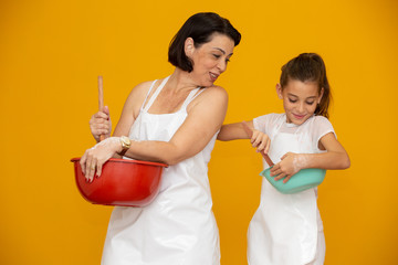 Mother's day concept! Daughter and mother preparing a recipe on yellow background