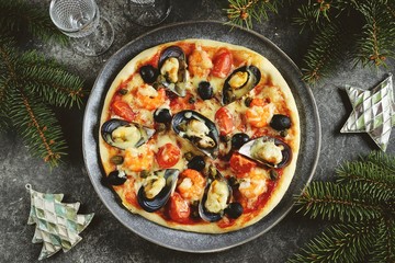 Delicious homemade pizza with seafood - mussels in shells, shrimp tails, capers and olives. Christmas background.