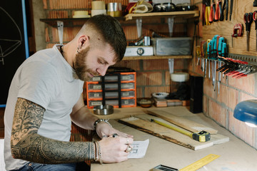 Bearded carpenter carefully drawing his project at craft workshop