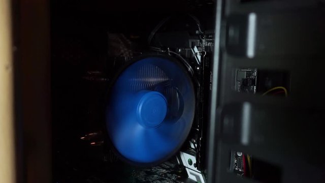 The cooling fan blades of the processor and motherboard are spinning in an open system unit, a case with RGB Light, while the computer is running. Evening, room, chip, microcircuit, backlight