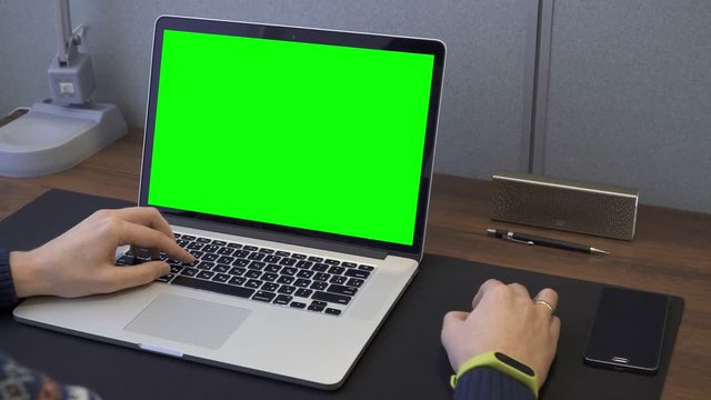 Man's hands on table with green screen laptop, computer mouse moving