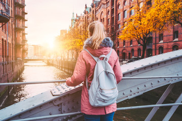Back rear view of adult blond woman tourist with backpack enjoying autumn beautiful sunset scene on...