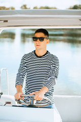 A young and handsome Caucasian man in glasses sailing in the sea on a boat on a sunny day.