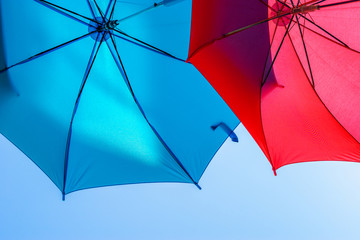 Two colorful umbrellas in the background of a sunny clear sky. Expanding blue and red umbrellas. Street decoration. Space for text.