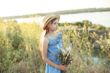Little girl in a straw hat with a bouquet of wildflowers on a background of a beautiful landscape