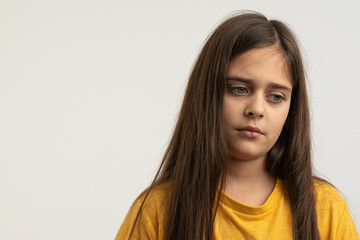 Fototapeta premium Waist up portrait of the upset, unhappy, sad brunette girl with loose hair, dressed in yellow t-shirt isolated over white background