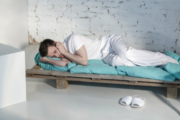 Obraz premium Young guy in white clothes depressed on a bed in a white room