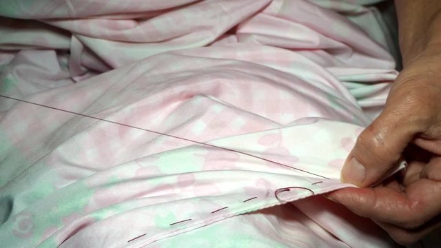 an adult woman seamstress sews impales the fabric with a needle. Hands close up. grandma makes a smooth hand stitch. Making clothes and sewing colored bed linen at home or in a garment factory