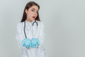 Lovely young doctor holding two small white pills in her palms, looking at the camera, not knowing...