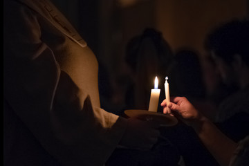 Woman in the traditionall religious habit dress in the church shares candle fire. Celebration of Lucia day in Sweden