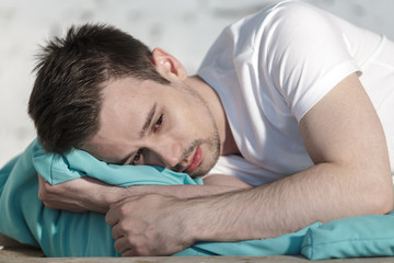 Young guy in white clothes depressed on a bed closeup