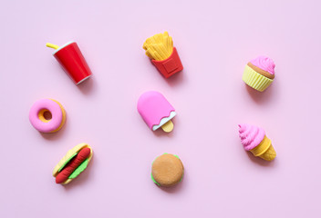 A variety of toy fast food and different sweets in miniature with shadows on a soft pink background.
